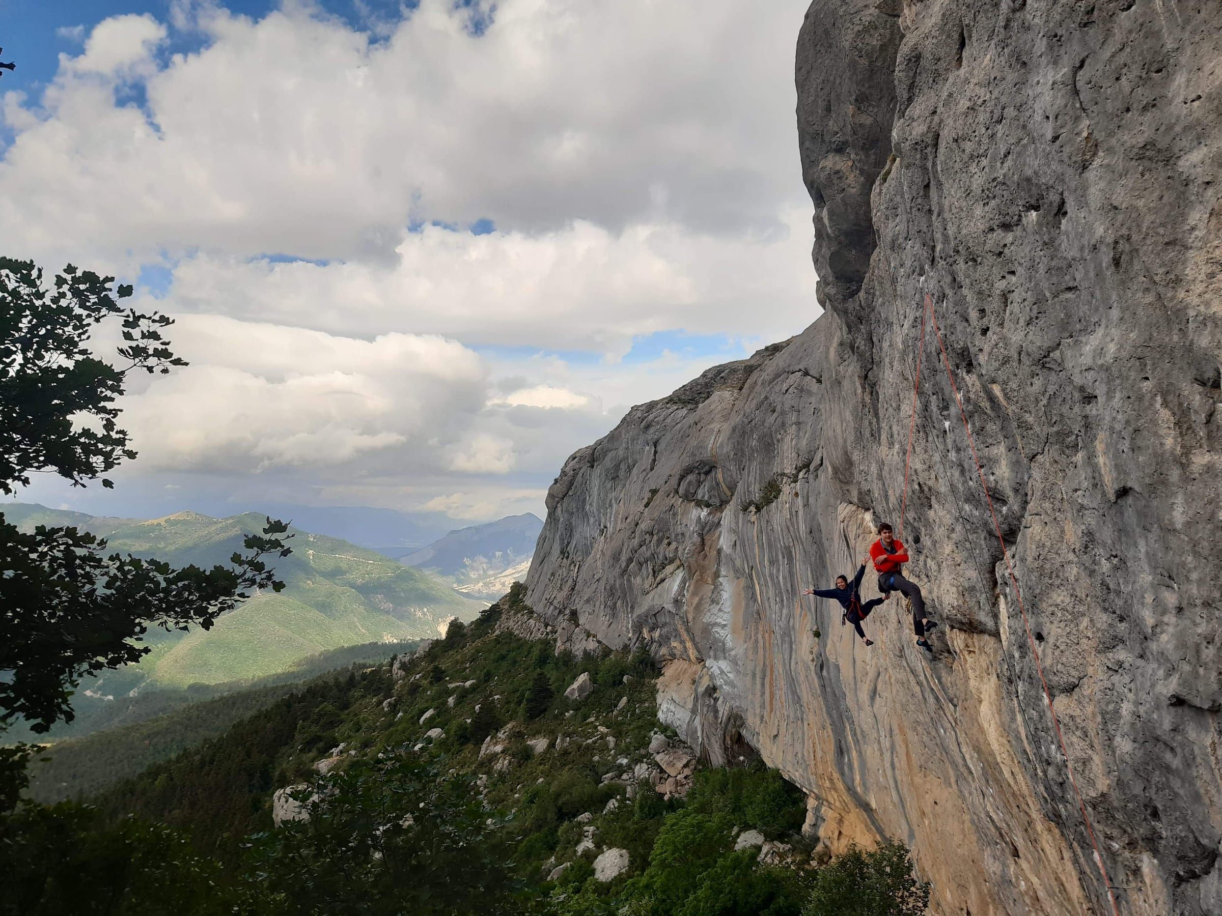A climber on a limestone crag above a green valley